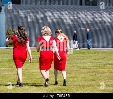 East Lothian, UK. 12th May, 2019. Wartime Experience: Women wearing red dresses, The Ragtime Dolls singers walking across a field Stock Photo