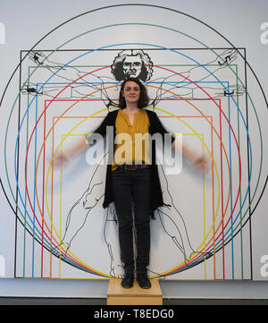 Hessen, Germany. 13 May 2019, Hessen, Gießen: Lisa Peter, employee of the interactive museum 'Mathematikum', stands in the permanent exhibition in front of the picture of the Leonardo man, a 'proportion study according to Vitruv'. Visitors can go in an exhibition to touch on the traces of Leonardo da Vinci. At around 20 stations and exhibits, they can try out whether the machines drawn by the Renaissance artist really work and what lies behind his ideas. Credit: dpa picture alliance/Alamy Live News Stock Photo