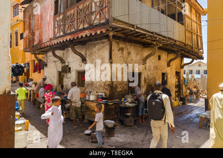 Locals preparing and cooking food in the shade of a building as children walk past, Mombasa old town, Kenya Stock Photo