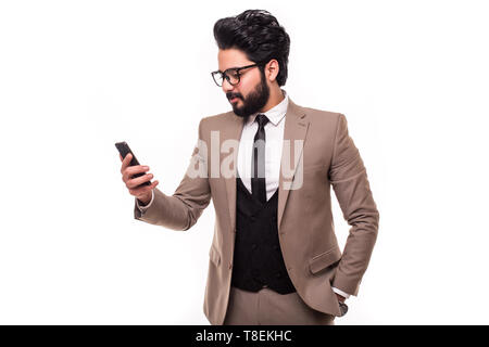 Businessman wearing a suit, holding his phone chatting looks shocked, isolated on white background. Stock Photo