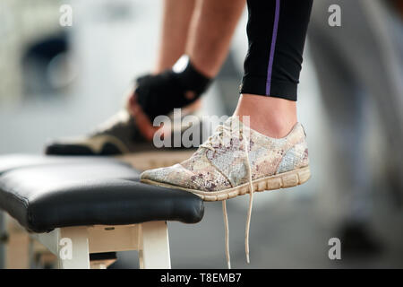 Female feet in sneakers in gym close up. Cropped image of womans leg in running shoes with untied laces at fitness club. People, fitness, active lifes Stock Photo