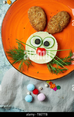 Kids menu, cutlets with mashed potatoes in the form of a hare's head on an orange plate on a gray background Stock Photo
