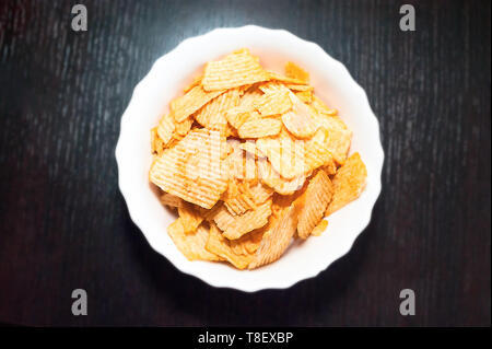Top-Down View of a White Bowl of Ridged Potato Chips on Dark Wooden Background. Stock Photo