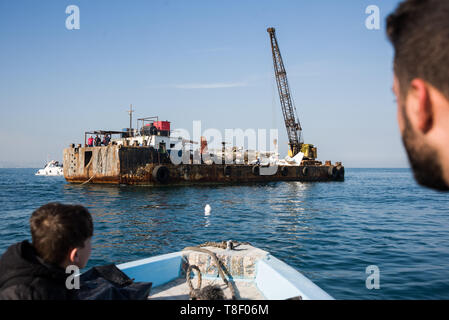 Members of the Sidoon Dive Academy seen watching as various light aircraft are carried out to sea on a barge during the project. Decommissioned aircrafts are winched into the water off the town of Saida in Lebanon as part of a conservation project to create an artificial reef. The sea floor here is barren, so the idea is to provide fish and invertebrates with permanent structures to give them a place to breed and shelter in order to increase fish and marine life stocks for fishing and tourism. Stock Photo