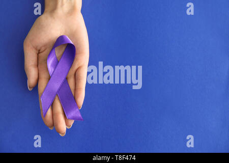 Woman holding purple ribbon on color background. Pancreatic cancer awareness concept Stock Photo