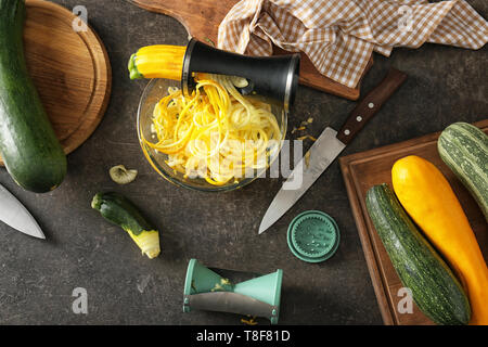 Fresh zucchini spaghetti with spiral grater and vegetables on dark table Stock Photo