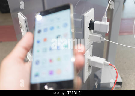 Female hands holding cell phone and using smartphone apps while charging it in a public place using electric plug and a charging cable. Focus on Stock Photo