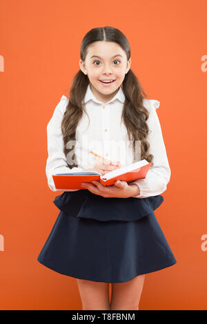 school diary for making notes. surprised small girl in school uniform. get information form book. schoolgirl writing notes on orange background. back to school. school reporter. reporter career. Stock Photo