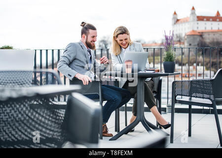 Two young business people with laptop sitting on a terrace outside office, working. Stock Photo