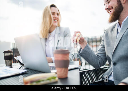 Businesspeople with laptop sitting on a terrace outside office, working and eating. Stock Photo