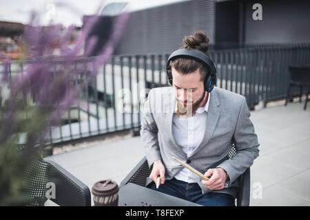 A young businessman with headphones sitting on a terrace, having fun. Stock Photo
