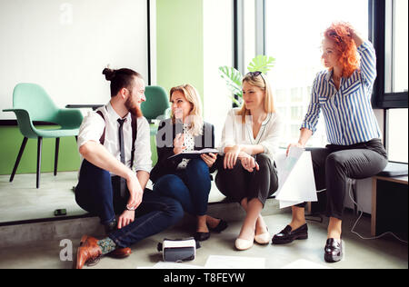 A group of young business people sitting on the floor in an office, talking. Stock Photo