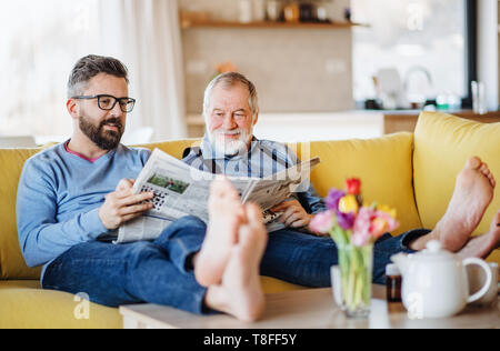 An adult hipster son and senior father sitting on sofa indoors at home, talking. Stock Photo