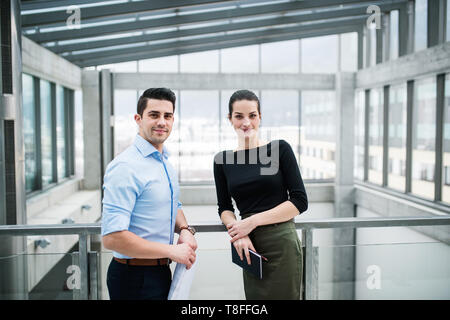Two young architects with blueprints standing in office, looking at camera. Stock Photo