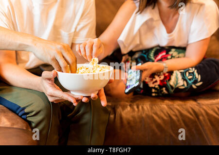 Hands taking popcorn from bowl watching movie with friends. Stock Photo