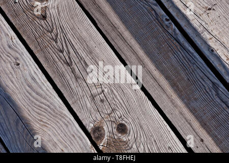 grey, worn, old and cracked wood planks of a boardwalk which have been exposed to weather and sun for years in a diagonal view Stock Photo