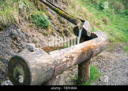 Natural raw unfiltered water flowing from wooden fountain spring at the Val Vertova torrent near Bergamo.Italy Stock Photo