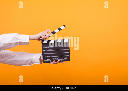 Shot of isolated hands on yellow background holding a clapper. Teenage girl holding clapper in studio. Stock Photo