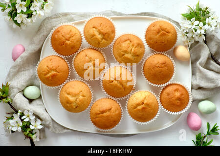 Springtime or Easter flat lay with plate of lemon muffins and marzipan eggs on light background with fresh apple flowers Stock Photo