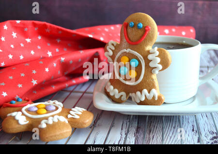 White cup of tea with a gingerbread man cookie, another gingerbread man with beautiful colorful sugar icing close by, red starred christmas fabric, wh Stock Photo