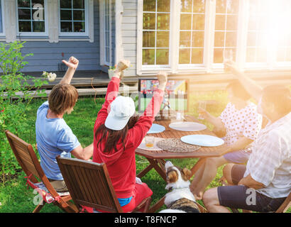 Happy family or company of friends watching football on TV in the courtyard of their home outdoors. Stock Photo