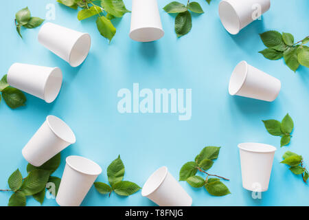Border of white disposable cup and green leaves on blue background. Save the planet. Zero waste. Top view Stock Photo