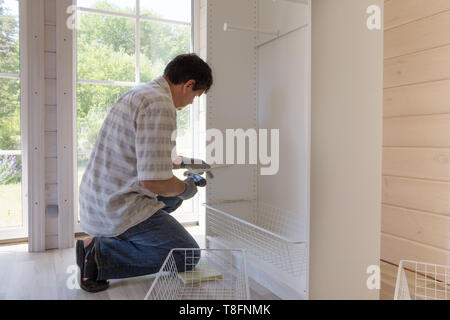The process of assembling furniture, the master assembles a white cabinet using an electric drill Stock Photo