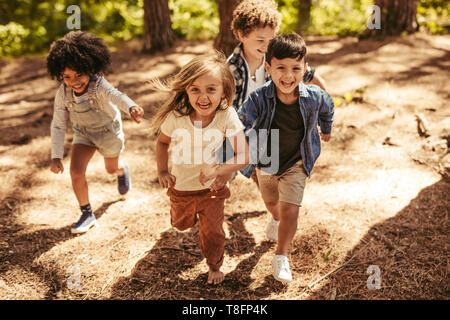 Group of four kids running together in the forest. Children having a race to climb up hill forest path. Stock Photo