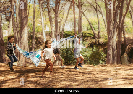 Four kids running in park with picnic blanket. Group of children enjoying together in park Stock Photo