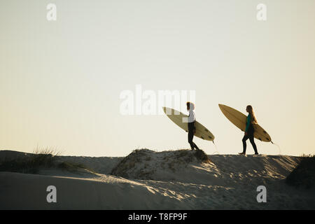 Two women surfers carrying surfboards and walking towards the sea. Female friends going on water surfing in the ocean.