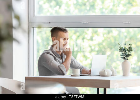 Troubled freelancer working on laptop in cafe Stock Photo