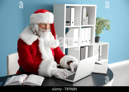 Santa Claus working on laptop at table Stock Photo