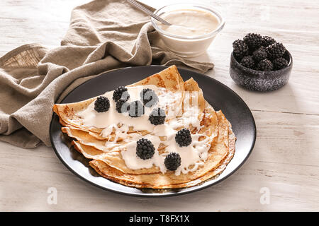 Plate with tasty thin pancakes, berries and sour cream on wooden table Stock Photo