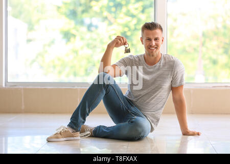 Happy young man with key from his new house indoors Stock Photo