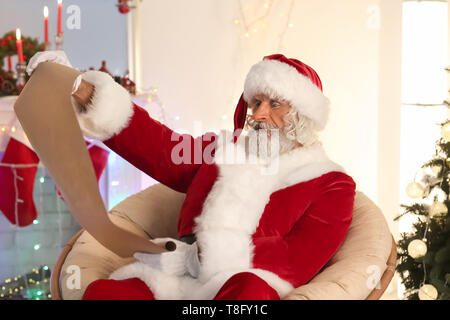 Santa Claus reading wish list in room decorated for Christmas Stock Photo
