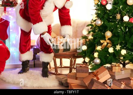 Santa Claus putting gifts under Christmas tree in room Stock Photo