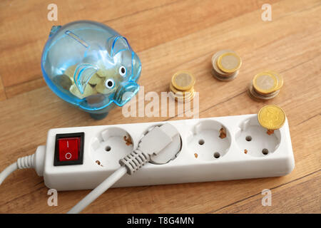 Piggy bank with coins and extension cord on floor. Electricity saving concept Stock Photo