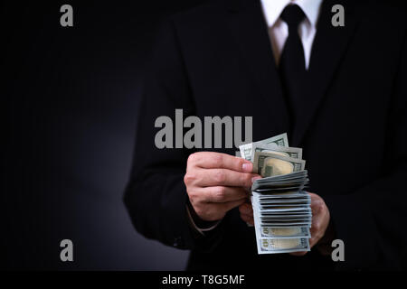 Businessman counts money in hand against dark background, US dollar (USD) bills - investment, success and profitable business concepts. Stock Photo