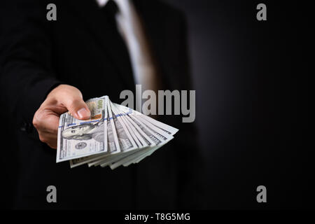 Businessman with money in hand and giving money as a bribe, US dollar (USD) bills - investment, success and profitable business concepts. Stock Photo