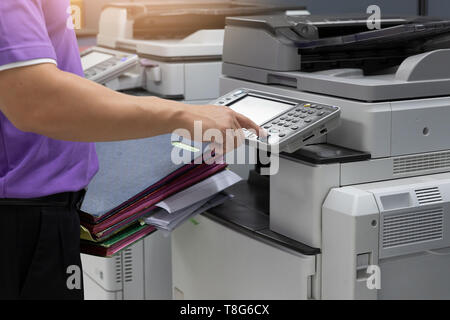 Bussinessman using copier machine to copy heap of paperwork in office. Stock Photo