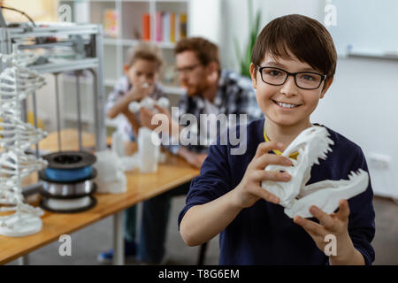 Beaming dark-haired boy in blue sweater carrying white 3d-model of head Stock Photo