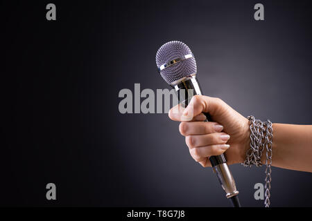 Woman hand with microphone tied with a chain, depicting the idea of freedom of the press or freedom of expression on dark background. World press free Stock Photo