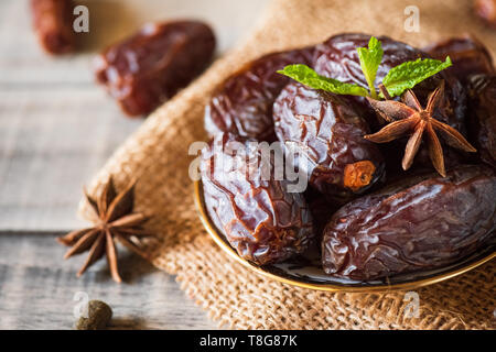 Ramadan food and drinks concept. Dates fruit and green Mint leaves in a bowl on wooden table background. Stock Photo