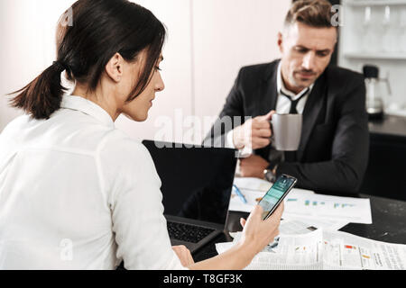 Two colleagues working on a project together while sitting at the office desk, using laptop, analyzing documents Stock Photo