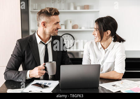 Two colleagues working on a project together while sitting at the office desk, using laptop, analyzing documents Stock Photo