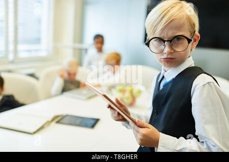 Boy as manager or CEO with tablet looks skeptically in the meeting Stock Photo