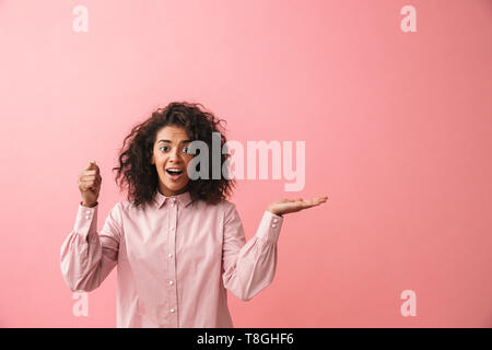 Image of a happy beautiful young african woman posing isolated over pink wall background showing copyspace imagine that she holding umbrella. Stock Photo