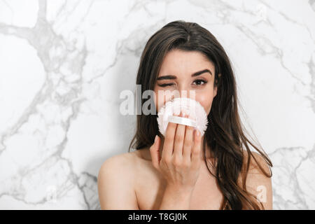 Beautiful young woman wrapped in a towel standing over marble background, using powder puff Stock Photo