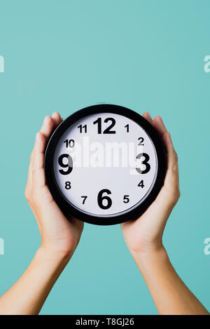 the hands of a young caucasian man holding a clock, without hour or minute hands, against a blue background, depicting concepts such as to not have ti Stock Photo