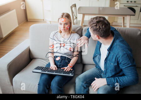 Young man and woman have social media addiction. Sitting on sofa. Hostages. Emotionless woman on sofa. Worried man touching her Stock Photo